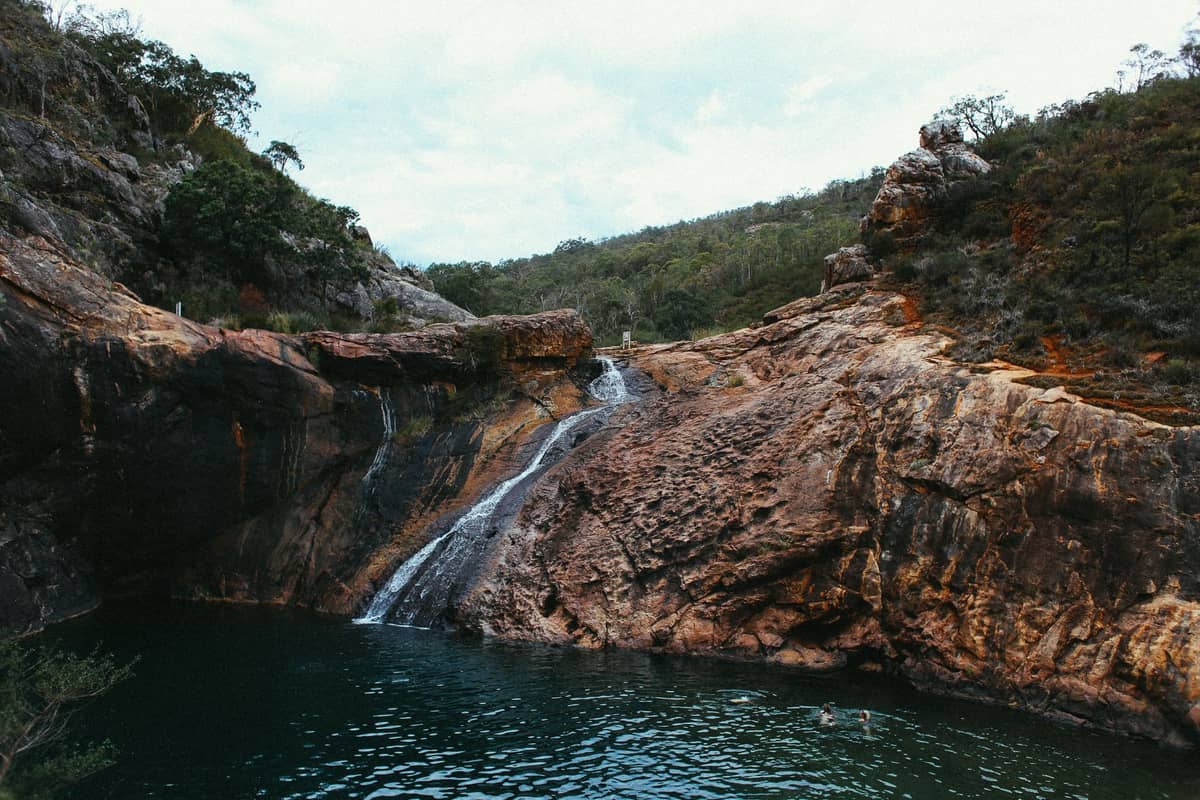 Natürliches Schwimmloch und kleiner Wasserfall, umgeben von felsigen Klippen und Grün, typisch für die Serpentine Falls in der Nähe von Perth.