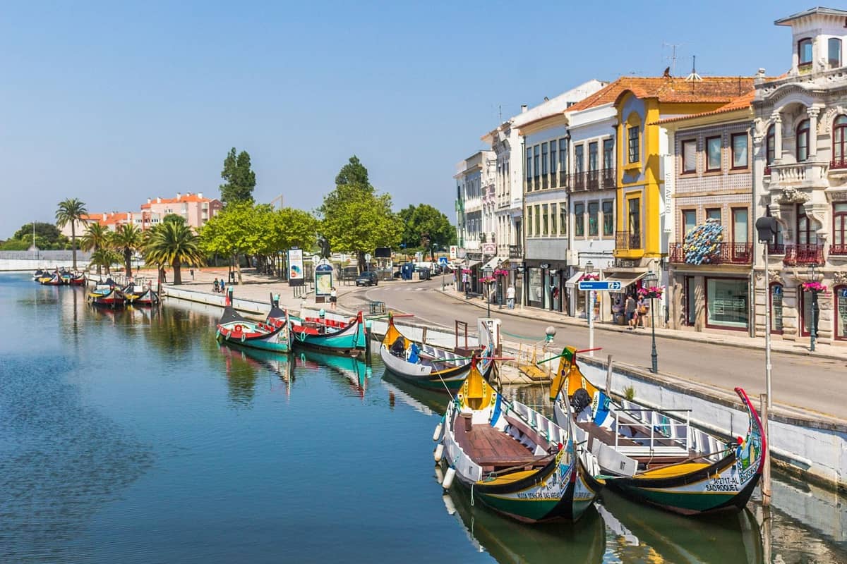 Bunte Moliceiro-Boote, die entlang eines Kanals mit Jugendstilgebäuden in Aveiro, Portugal, an einem sonnigen Tag angelegt haben.