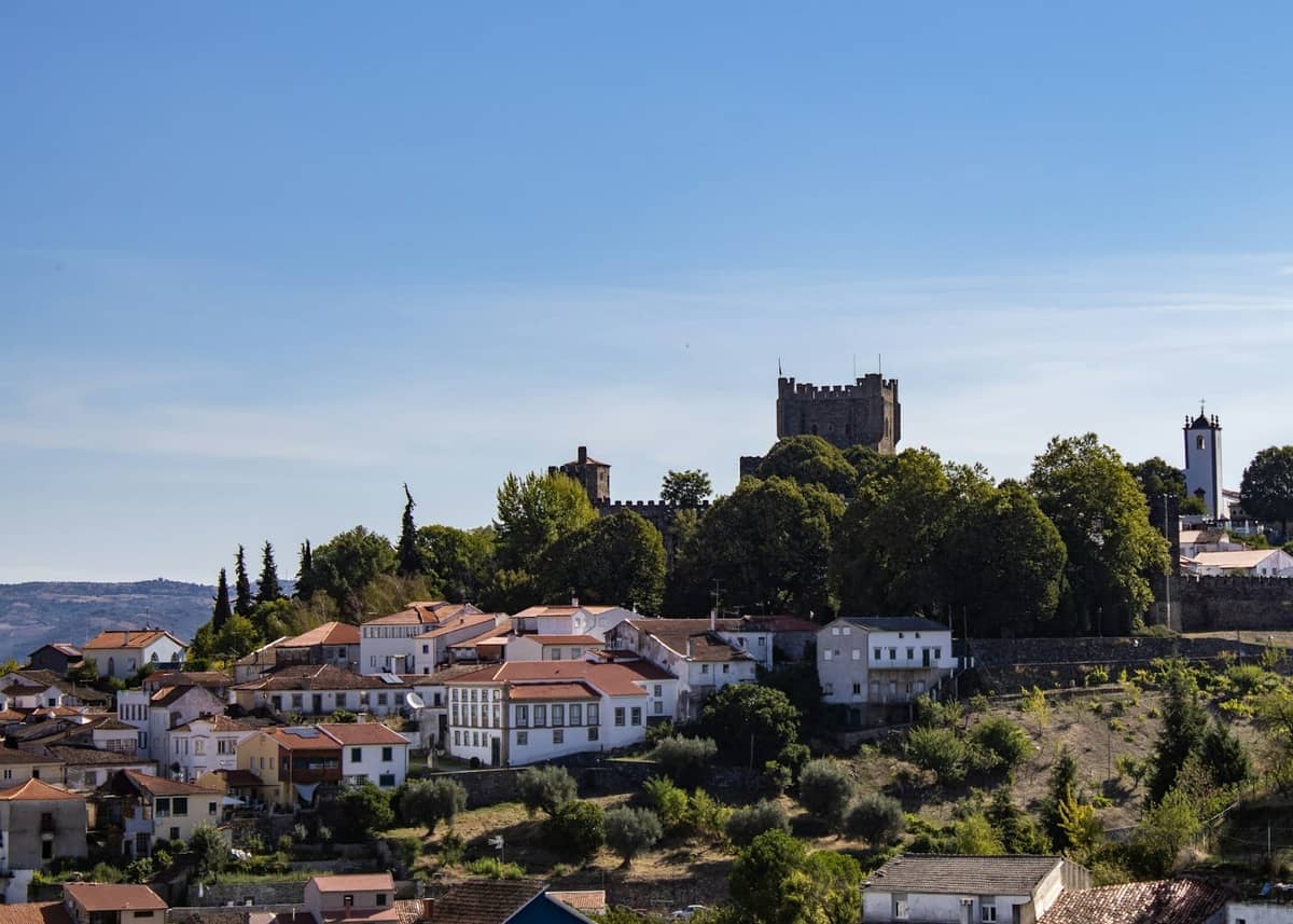 Mittelalterliche Burg auf einem Hügel, die sich über weiß getünchte Häuser und Bäume in einer portugiesischen Stadtlandschaft unter blauem Himmel erhebt