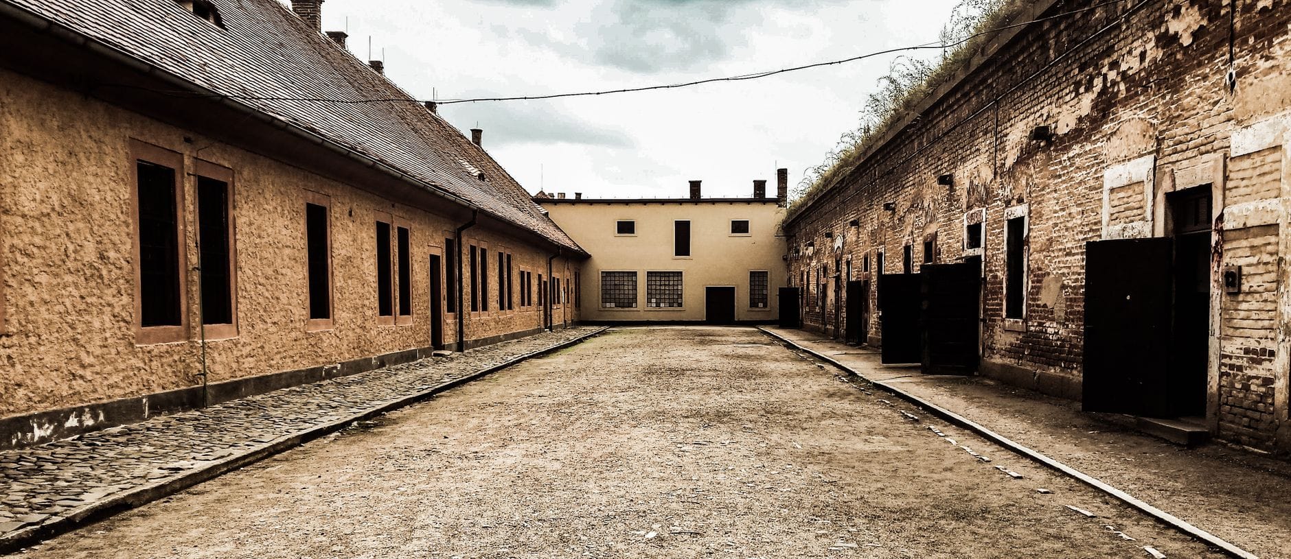 Cortile storico tra gli edifici del carcere con finestre con sbarre e porte aperte, sotto un cielo nuvoloso nel sito memoriale di Terezín vicino a Praga.