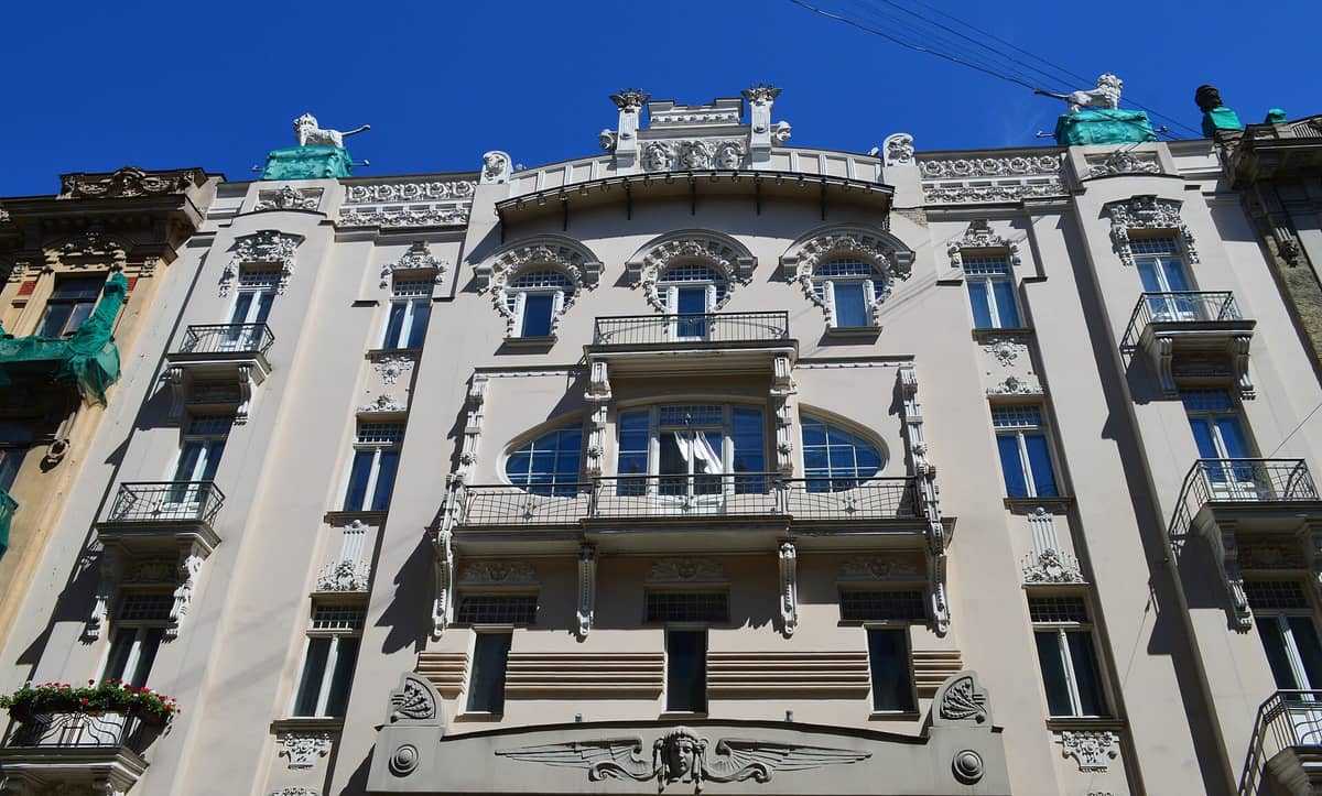 Verzierte Jugendstil-Gebäudefassade in Riga, Lettland, mit Balkonen, dekorativen skulpturalen Details und einem strahlend blauen Himmel.