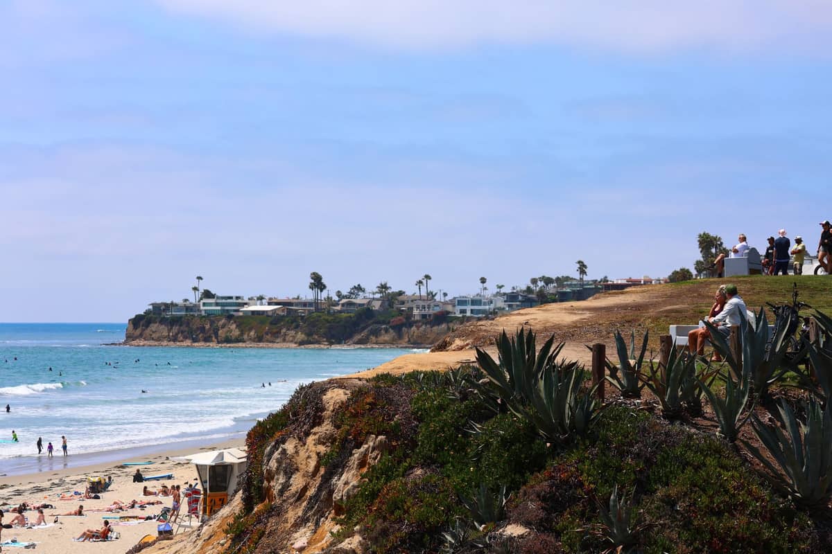 Blick auf eine Küstenklippe und einen Sandstrand in North County mit Menschen, die sich sonnen, surfen und in der Nähe von Carlsbad oder Encinitas entspannen.