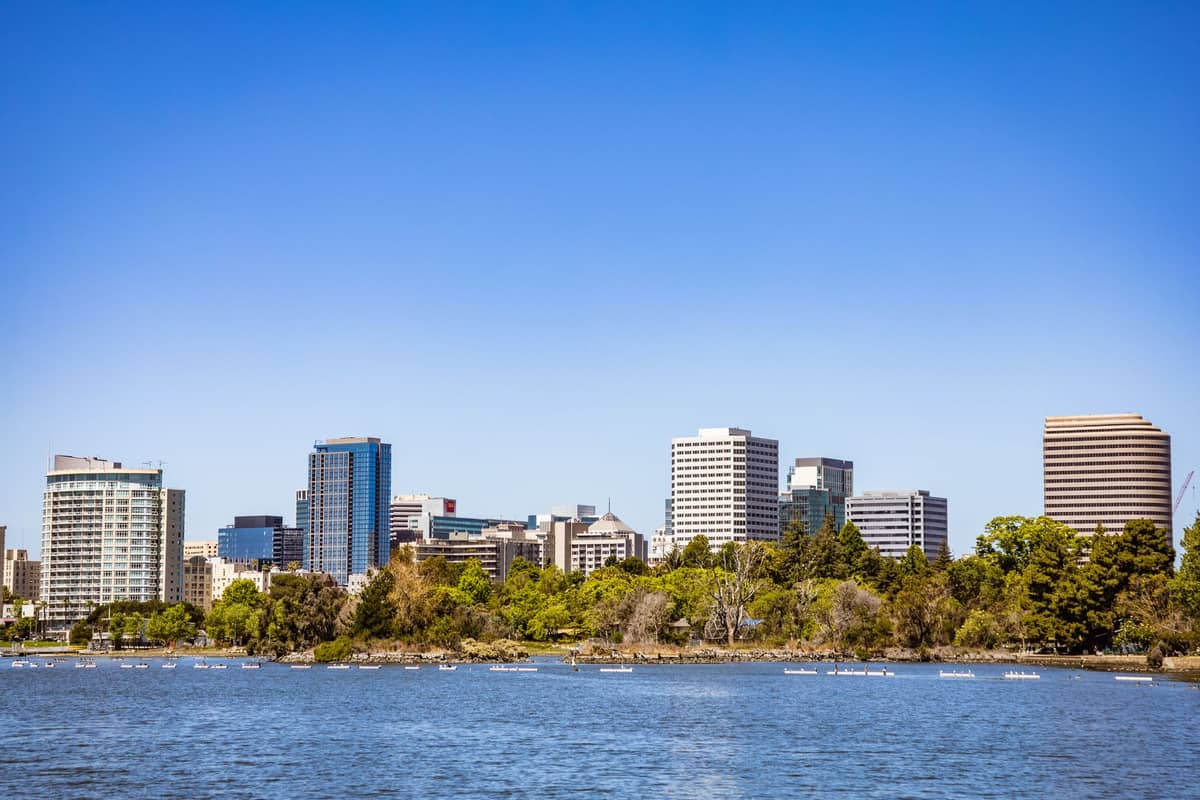 Vista dello skyline del centro di Oakland con moderni edifici per uffici e alberi lungo le rive del Lake Merritt sotto un cielo azzurro limpido.