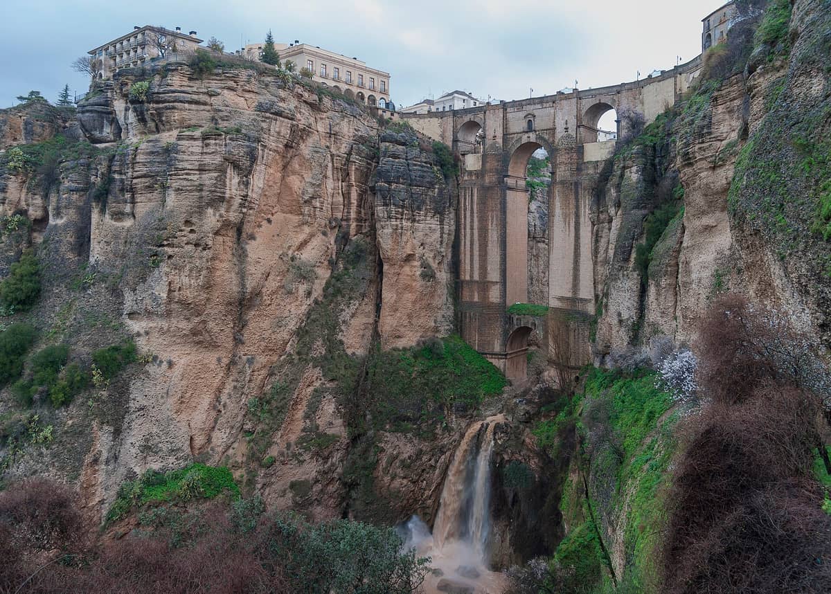 ทิวทัศน์อันตระการตาของสะพาน Puente Nuevo ในเมือง Ronda ที่พาดข้ามหุบเขาลึกพร้อมน้ำตก ล้อมรอบด้วยหน้าผาหินและอาคารประวัติศาสตร์ด้านบน