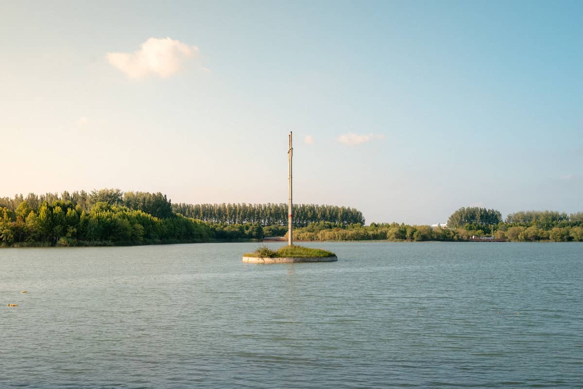 Un río tranquilo con una pequeña isla y un solitario poste alto, rodeado de un exuberante bosque bajo un cielo azul cerca de Shanghai.