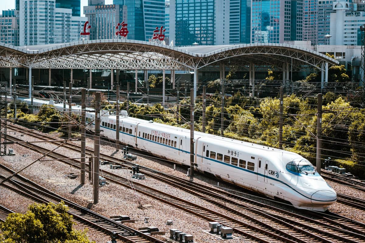 Un moderno tren bala de alta velocidad en la estación de ferrocarril de Shanghai con rascacielos de la ciudad al fondo, mostrando excelentes conexiones de transporte.