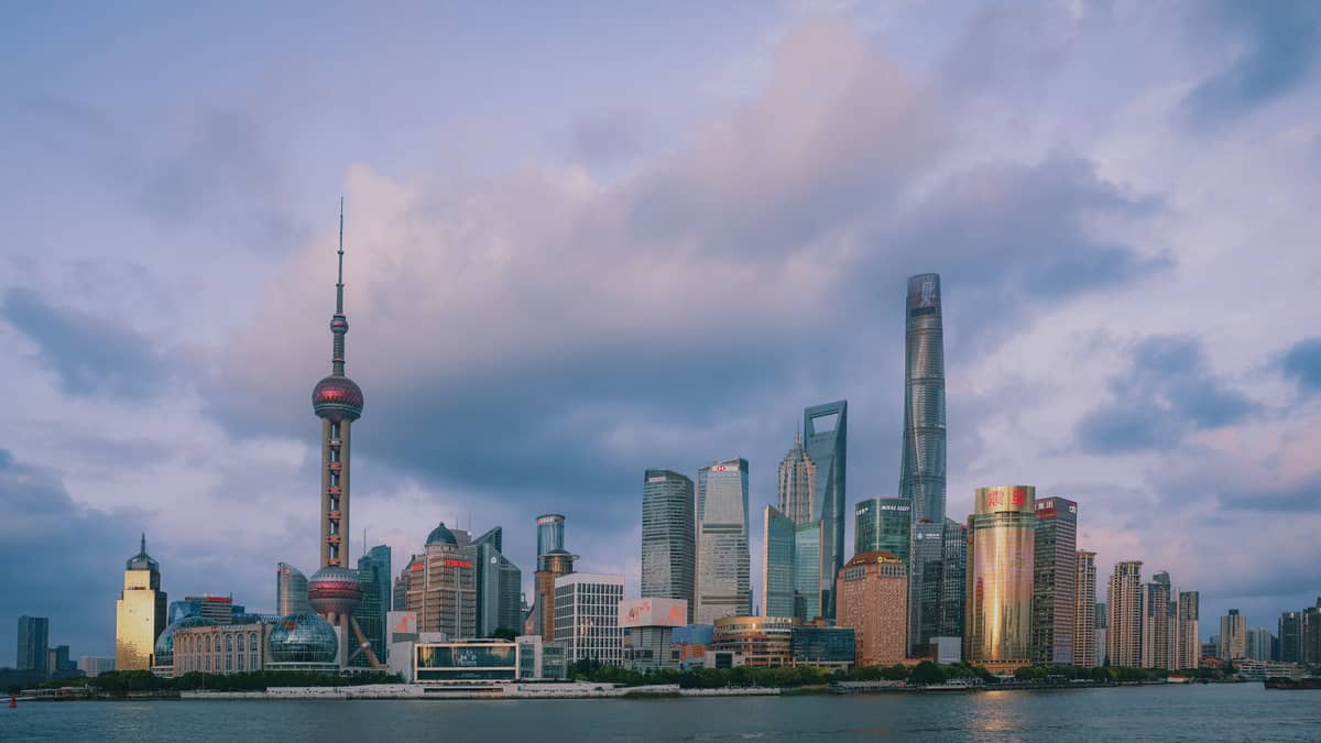 Skyline von Shanghai mit dem Oriental Pearl Tower und modernen Wolkenkratzern, vom Huangpu-Fluss aus unter einem dramatisch bewölkten Abendhimmel fotografiert.