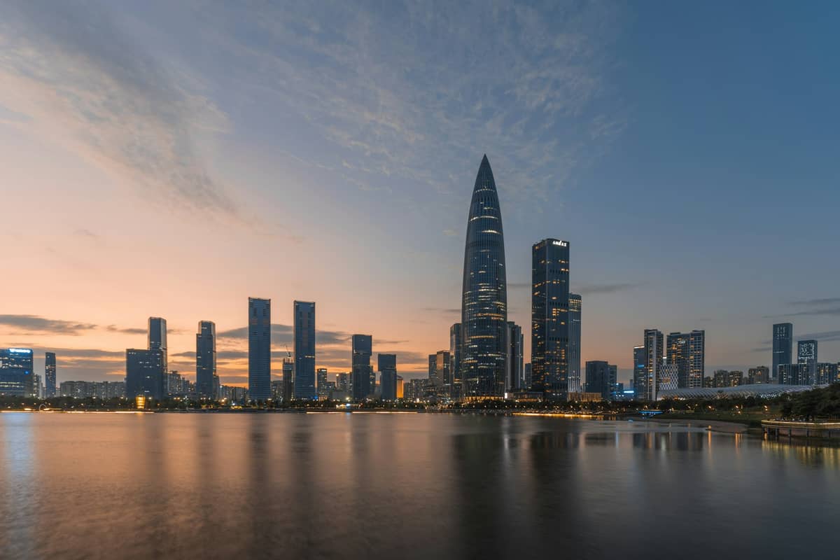Vista panorâmica do horizonte de Shenzhen ao pôr do sol, com o icônico edifício da China Resources e os arranha-céus modernos refletidos na baía.