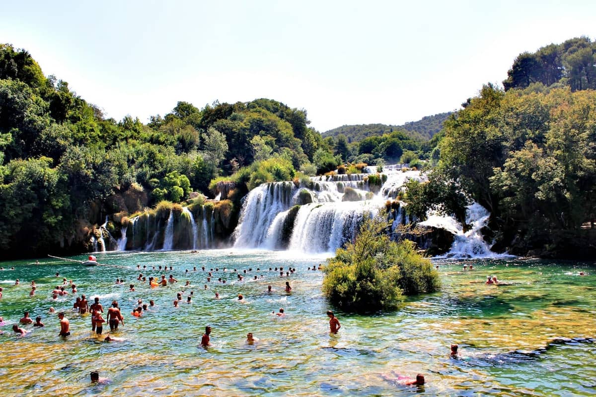 Molte persone che nuotano e guadano davanti alla cascata Skradinski Buk nel Parco Nazionale di Krka in una giornata di sole.