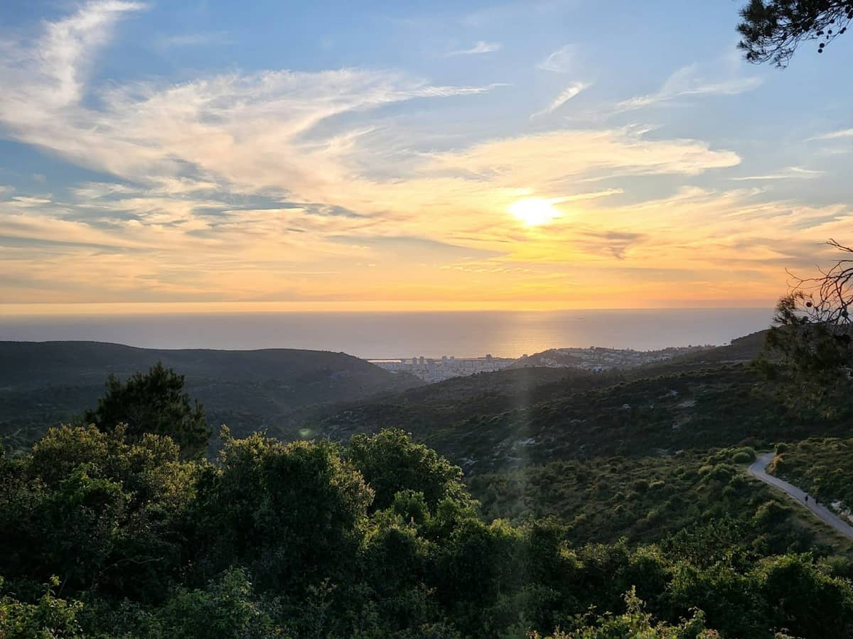 Malerischer Blick auf üppige Hügel und Küste bei Sonnenuntergang mit einem gewundenen Pfad und der Stadt in der Ferne, Split, Kroatien