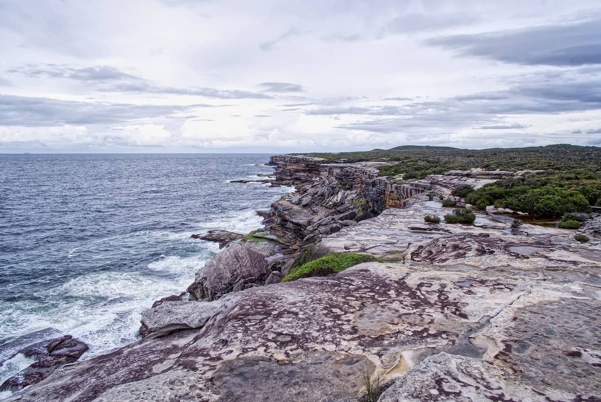 Costa rocosa espectacular y acantilados oceánicos con vegetación arbustiva en el Royal National Park al sur de Sídney en un día nublado