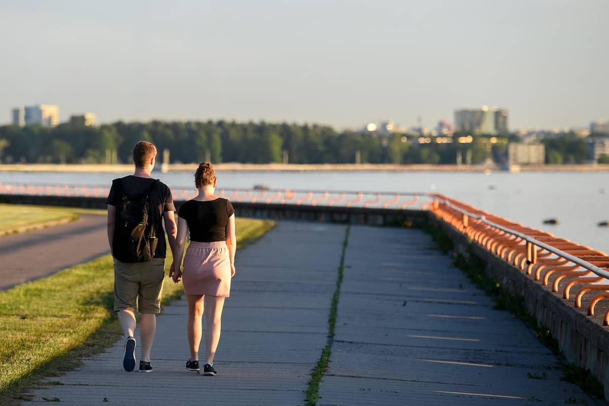 Una pareja pasea por un paseo marítimo con una vista lejana del horizonte de Tallinn y aguas tranquilas en una tarde despejada.