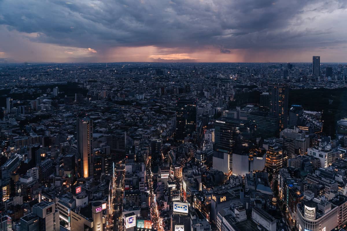A dramatic aerial landscape of Tokyo at dusk with a glowing city and Mount Fuji faint on the distant horizon, hinting at day trips beyond the city.