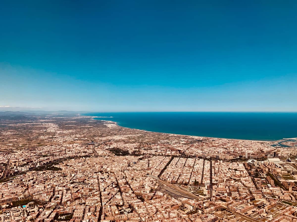 Luftpanoramamblick auf die Stadt Valencia mit Küstenlinie, Mittelmeer und umliegenden Ebenen unter einem klaren blauen Himmel.