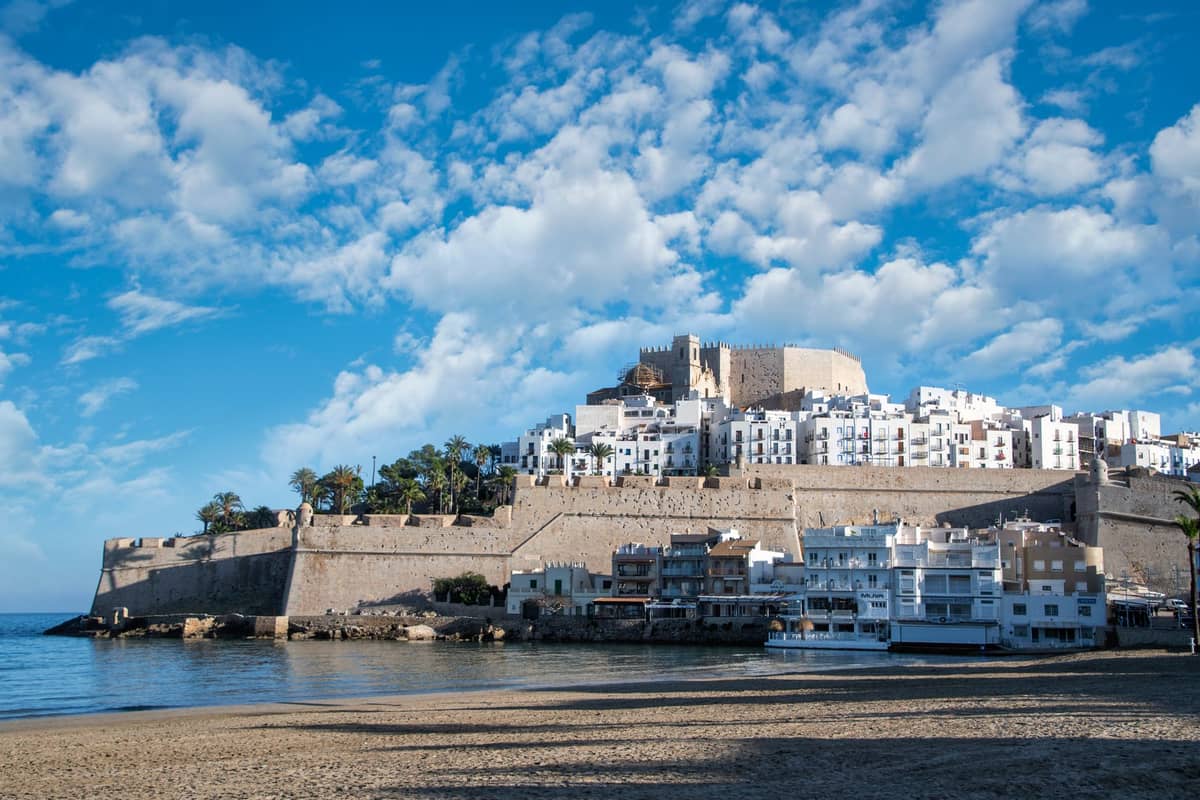 Blick auf Peñíscolas ummauerte Altstadt und die Burg, die sich an einem sonnigen Tag über weiße Gebäude und das Mittelmeer erhebt.