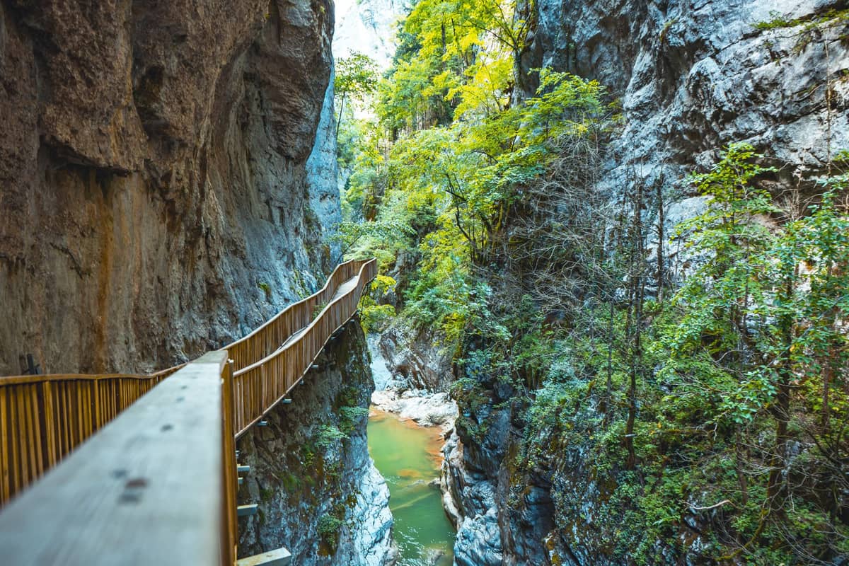 Hölzerner Gehweg durch eine dramatische felsige Schlucht mit einem Fluss unten und üppigem Grün an den Klippen.