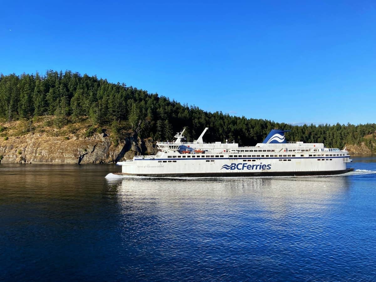 Ein Schiff der BC Ferries fährt nahe einer bewaldeten Insel unter klarem blauem Himmel, mit zerklüfteter Küstenlinie und tiefblauem Wasser im Gulf of Georgia.
