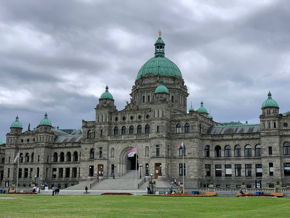 Die historischen British Columbia Parliament Buildings mit Kuppeldächern und einem Rasen davor unter einem bewölkten Himmel in Victoria, Vancouver Island.