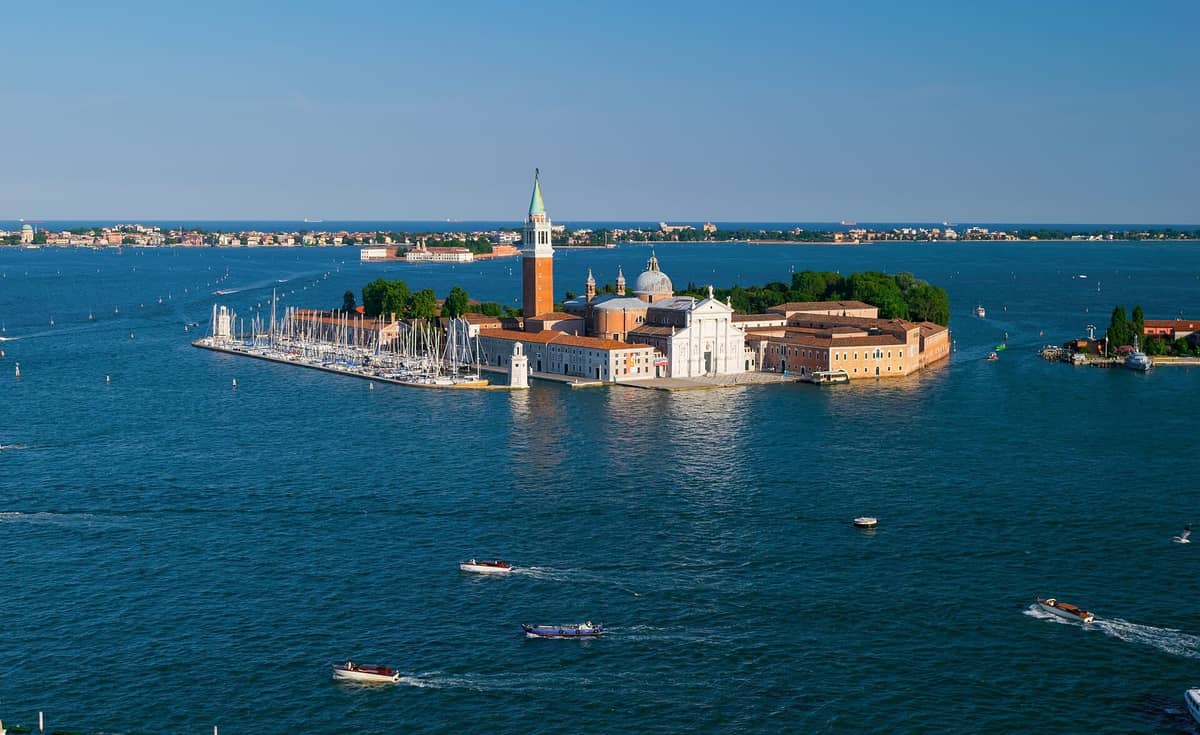 มุมมองทางอากาศของเกาะ San Giorgio Maggiore แสดงให้เห็นโบสถ์ หอระฆัง มาริน่า และทะเลสาบ Venetian Lagoon พร้อมเรือในวันที่แดดส่อง