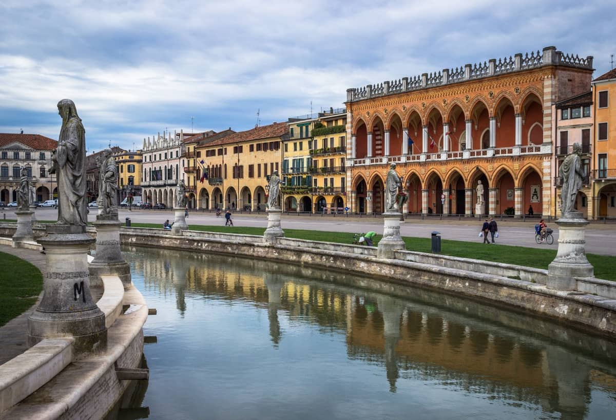 มุมมองกว้างของจัตุรัส Prato della Valle ในเมือง Padua พร้อมรูปปั้นเรียงรายตามคลองกลางและอาคารประวัติศาสตร์ในพื้นหลัง