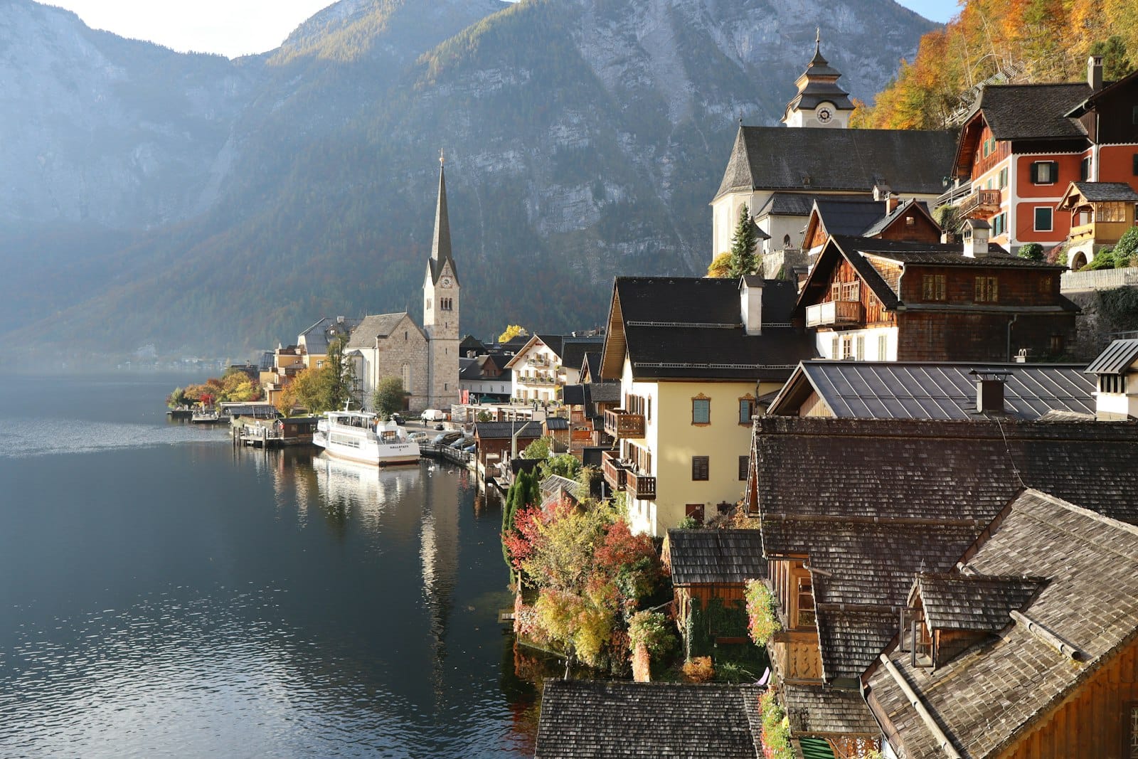 Pintoresco pueblo a orillas del lago de Hallstatt con casas alpinas tradicionales, un campanario y montañas reflejadas en las tranquilas aguas del Hallstätter See.