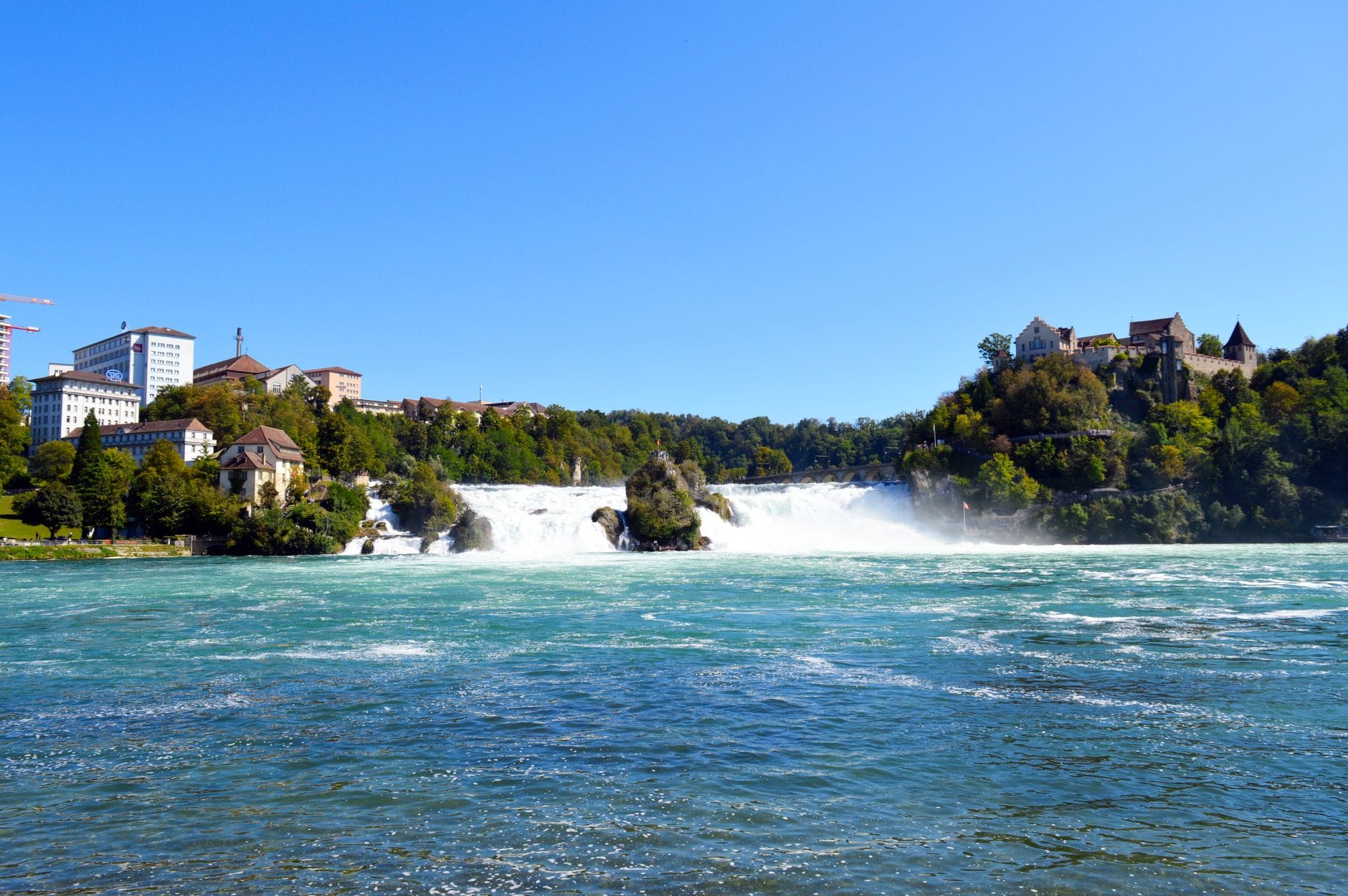 วิวทิวทัศน์กว้างของ Rhine Falls พร้อมอาคารประวัติศาสตร์ทั้งสองฝั่งและหมอกที่ลอยขึ้นเหนือน้ำตกที่ใหญ่ที่สุดในยุโรป ใกล้เมือง Schaffhausen ประเทศสวิตเซอร์แลนด์