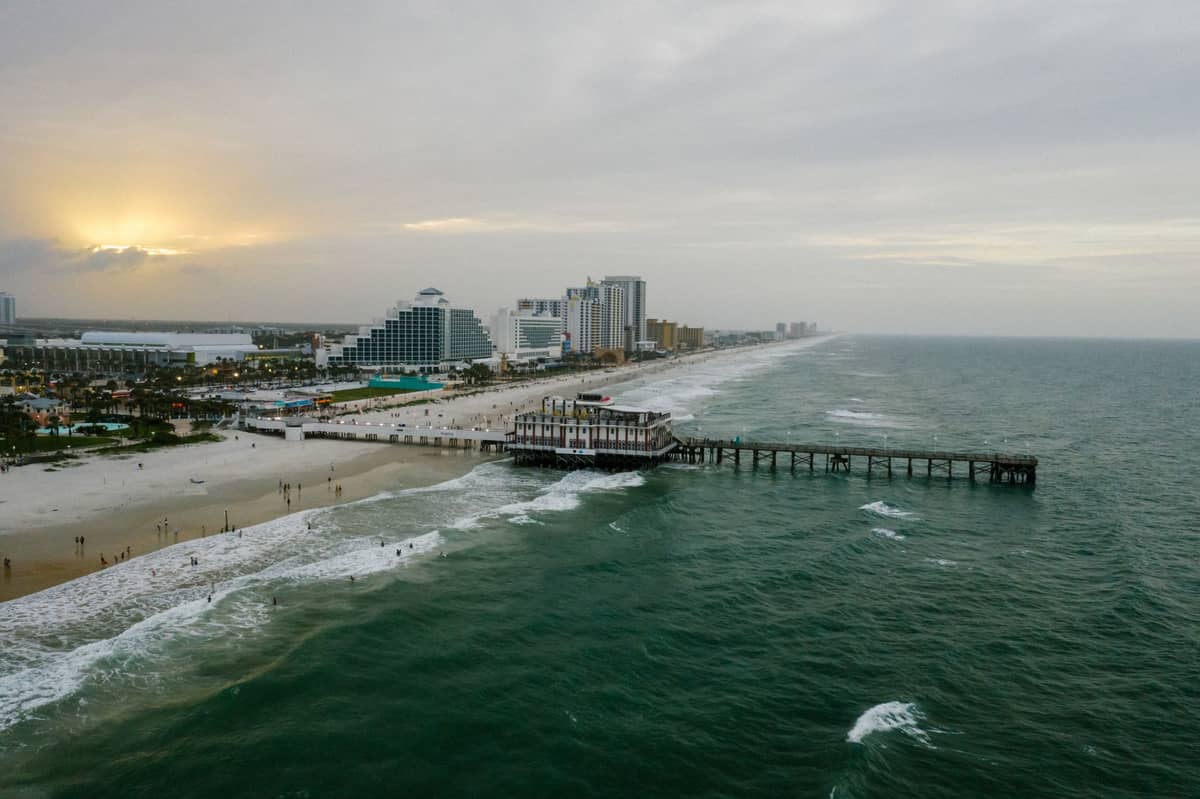 Luftaufnahme der Daytona Beach Küstenlinie mit dem historischen Main Street Pier, Strandhotels und dem Atlantik im Sonnenuntergang.