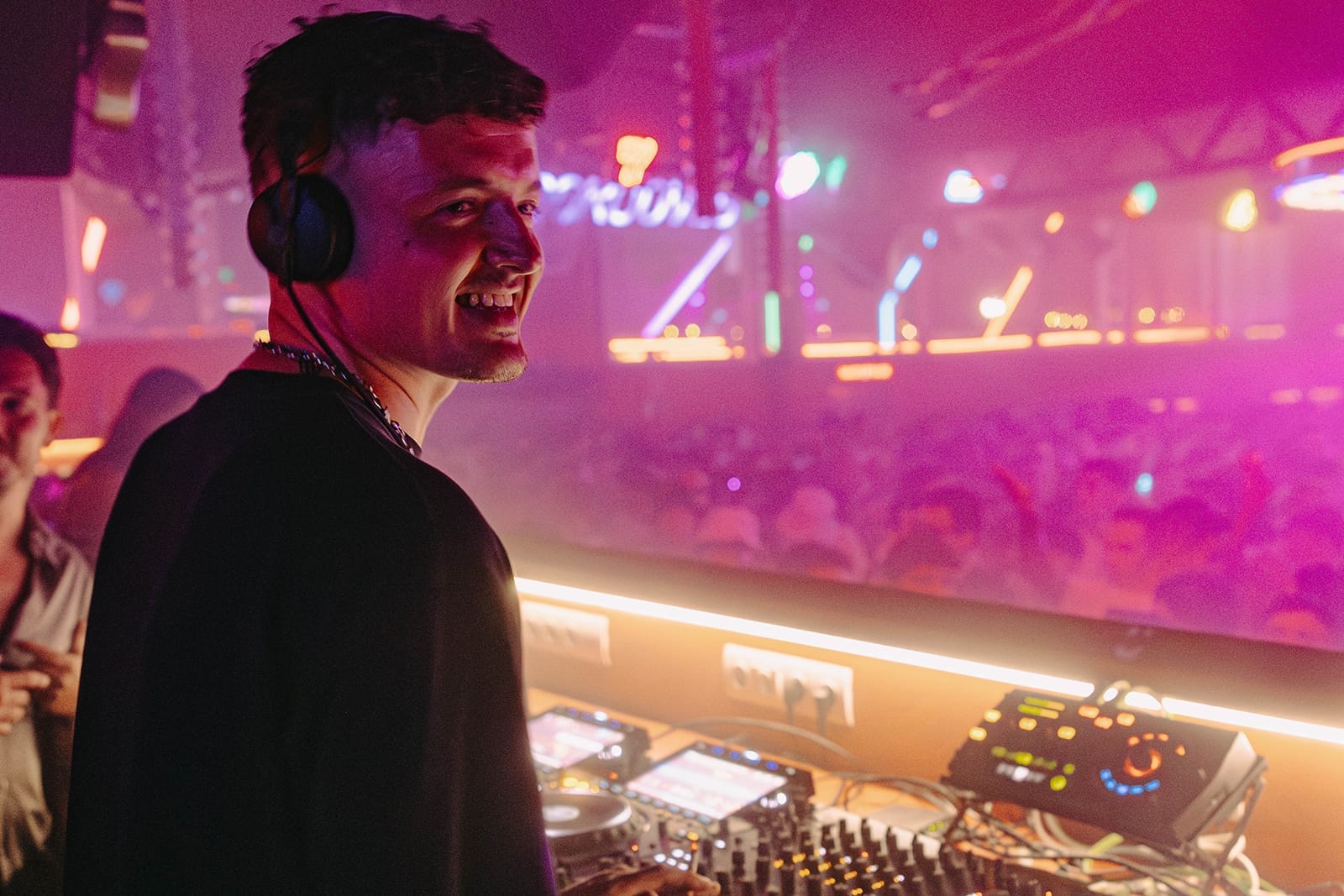 DJ che si esibisce al DC10 Ibiza con una folla che balla sotto luci al neon colorate e un'atmosfera nebbiosa da club sullo sfondo.