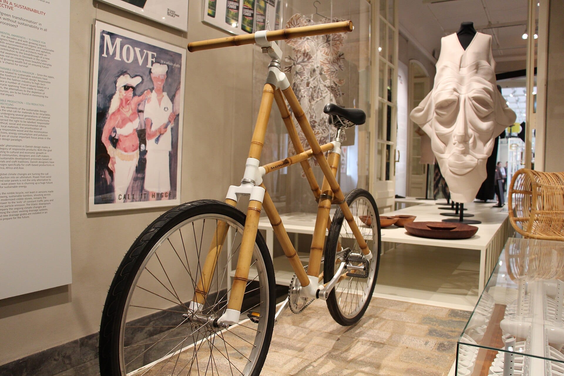 Una bicicletta di bambù è esposta tra oggetti di arte moderna e design al Designmuseum Danmark a Copenaghen, con illuminazione interna soffusa e interni dettagliati.