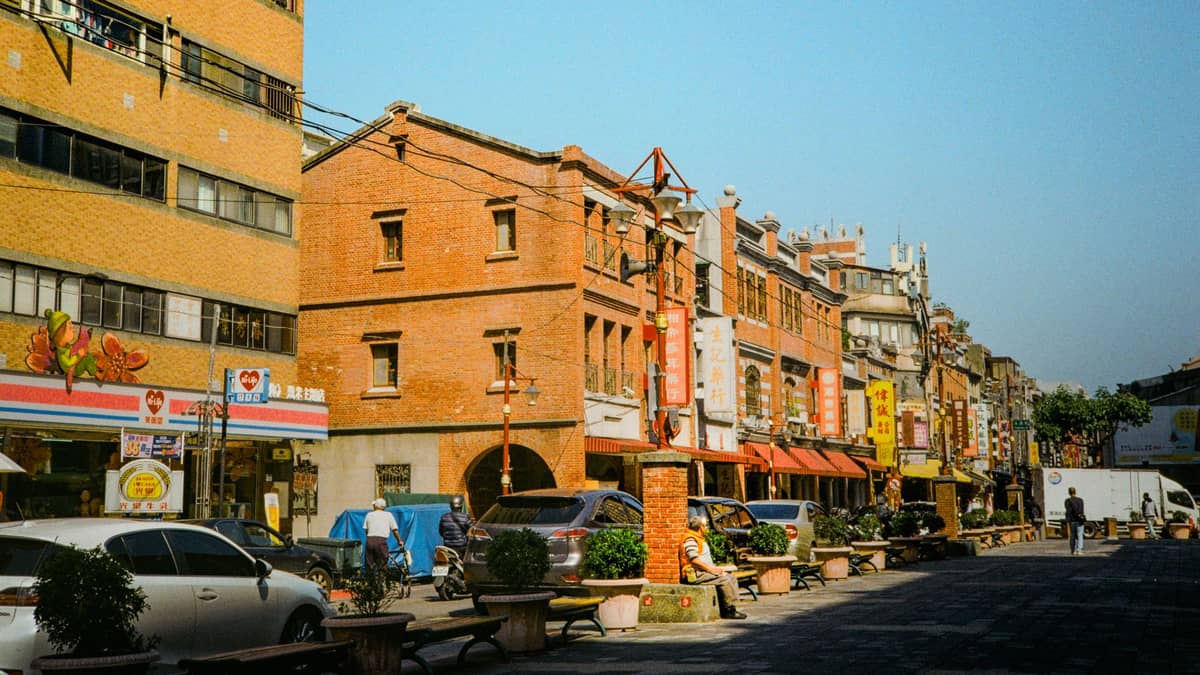 Weitwinkelaufnahme der Dihua Street in Taipei mit historischen Backsteinläden, roten Laternen, Schildern und Straßenleben an einem sonnigen Tag.
