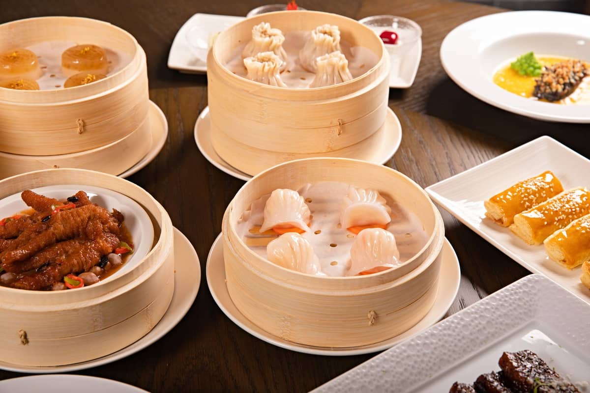 Assorted dim sum in bamboo steamers on a table, including dumplings, har gow, chicken feet, and other classic Cantonese dishes.