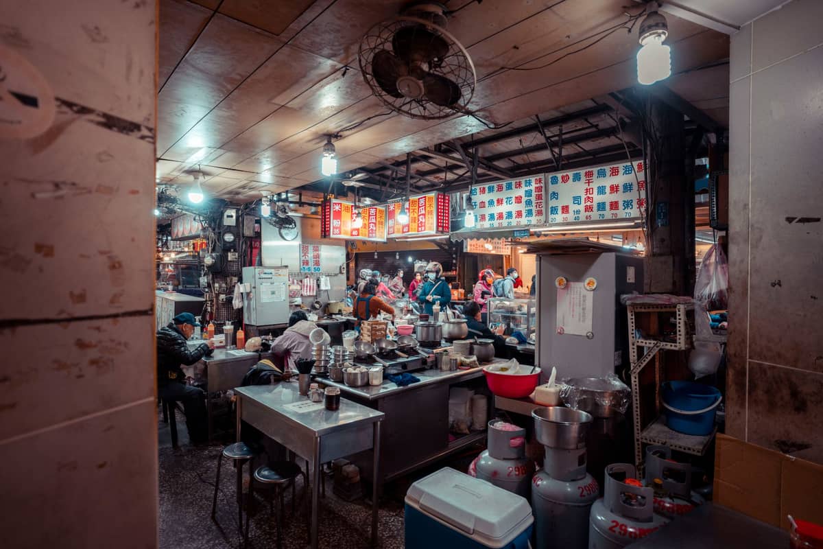 A bustling, casual Chinese restaurant with diners eating, kitchen equipment visible, and colorful menus on the wall, evoking a classic Guangzhou dim sum scene.