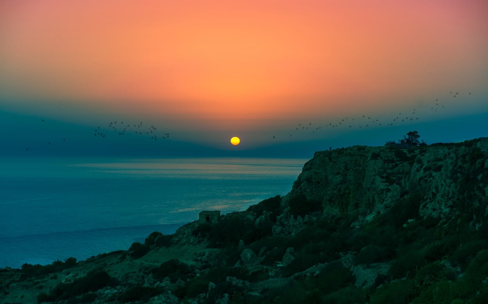 Tramonto spettacolare sulle Scogliere di Dingli con il sole che scende sul mare, i profili scuri delle rocce e un cielo coloratissimo.