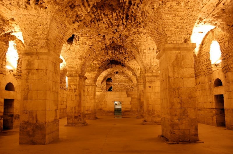 ซุ้มโค้งและเสาหินภายใน Diocletian's Cellars ในเมือง Split สว่างไสวด้วยแสงไฟอบอุ่น แสดงให้เห็นสถาปัตยกรรมโรมันโบราณ