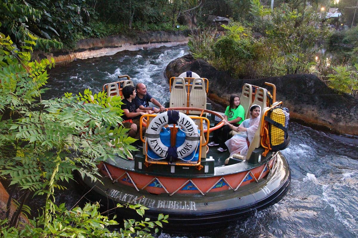 A raft with guests riding the Kali River Rapids attraction at Disney's Animal Kingdom, surrounded by lush greenery and flowing water.