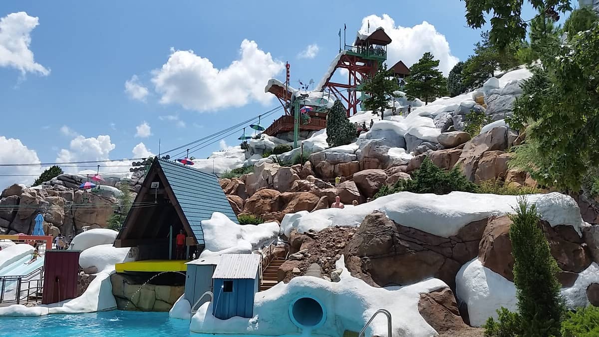 Disney's Blizzard Beach Wasserpark mit schneegestalteten Gebäuden, felsigen Hängen und Rutschen unter einem strahlend blauen Himmel mit vereinzelten Wolken.
