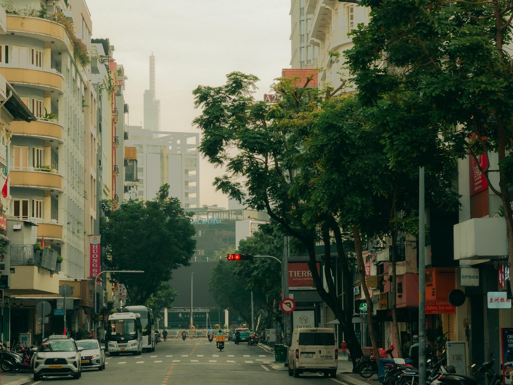Una tranquila calle arbolada en el Distrito 3 de Ciudad Ho Chi Minh, con edificios coloniales franceses, tiendas locales y motocicletas en una tarde apacible.