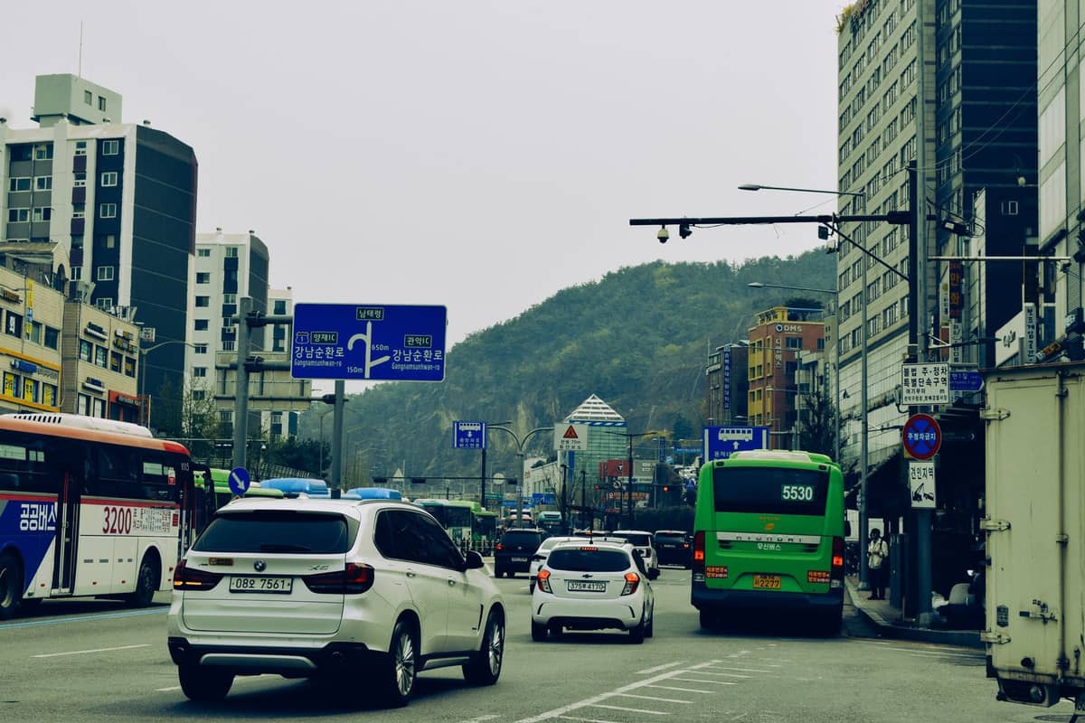 Cena de rua em Seul com tráfego, ônibus, carros, placas de ônibus azuis em coreano e colinas distantes nos arredores da cidade