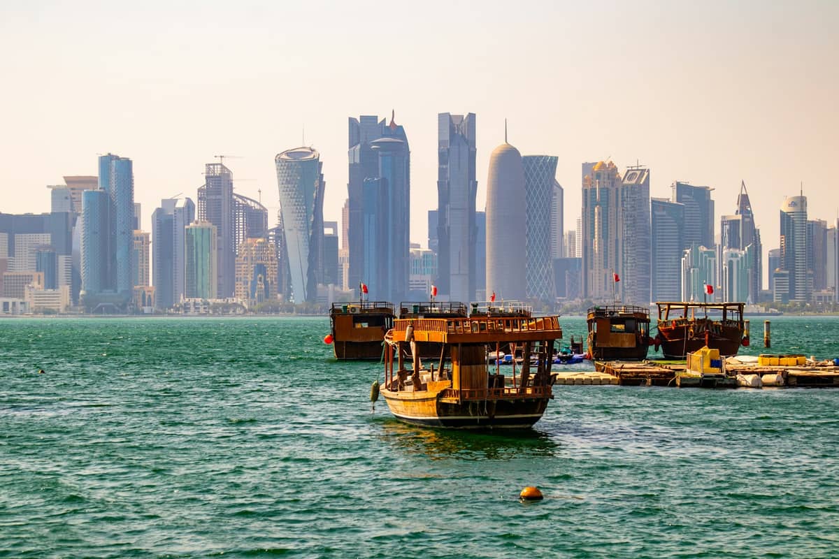 Traditionelle Dhau-Boote auf dem Wasser mit Dohas moderner West-Bay-Skyline im Hintergrund – ein Blick auf das Ufergebiet der Stadt und seine Bootsaktivitäten.