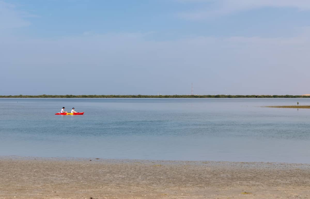 Zwei Personen beim Kajakfahren auf ruhigem, flachem Wasser mit Mangroven und blauem Himmel im Hintergrund, als Sinnbild für naturnahe Wassererlebnisse.