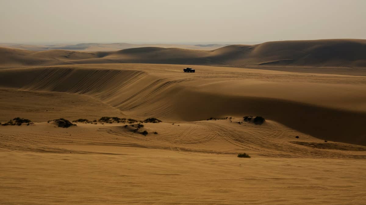 Ein einzelner SUV fährt über geschwungene Sanddünen unter einem dunstigen Wüstenhimmel in der Nähe von Doha, Katar.