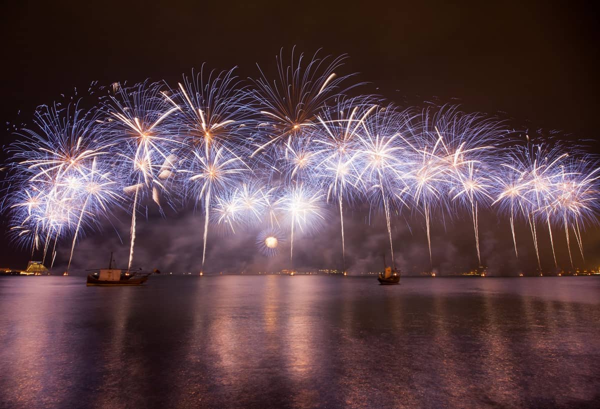 Großes nächtliches Feuerwerk über der Bucht von Doha mit traditionellen Booten auf dem Wasser, das eine festliche Feierstimmung widerspiegelt.
