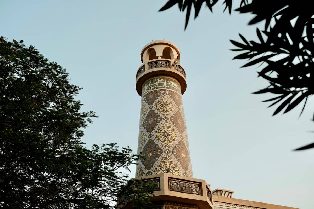 Dekorativ gemustertes Moschee-Minarett in Doha von unten gesehen, mit aufwendigen geometrischen islamischen Mustern und Laub, das die Ansicht einrahmt.