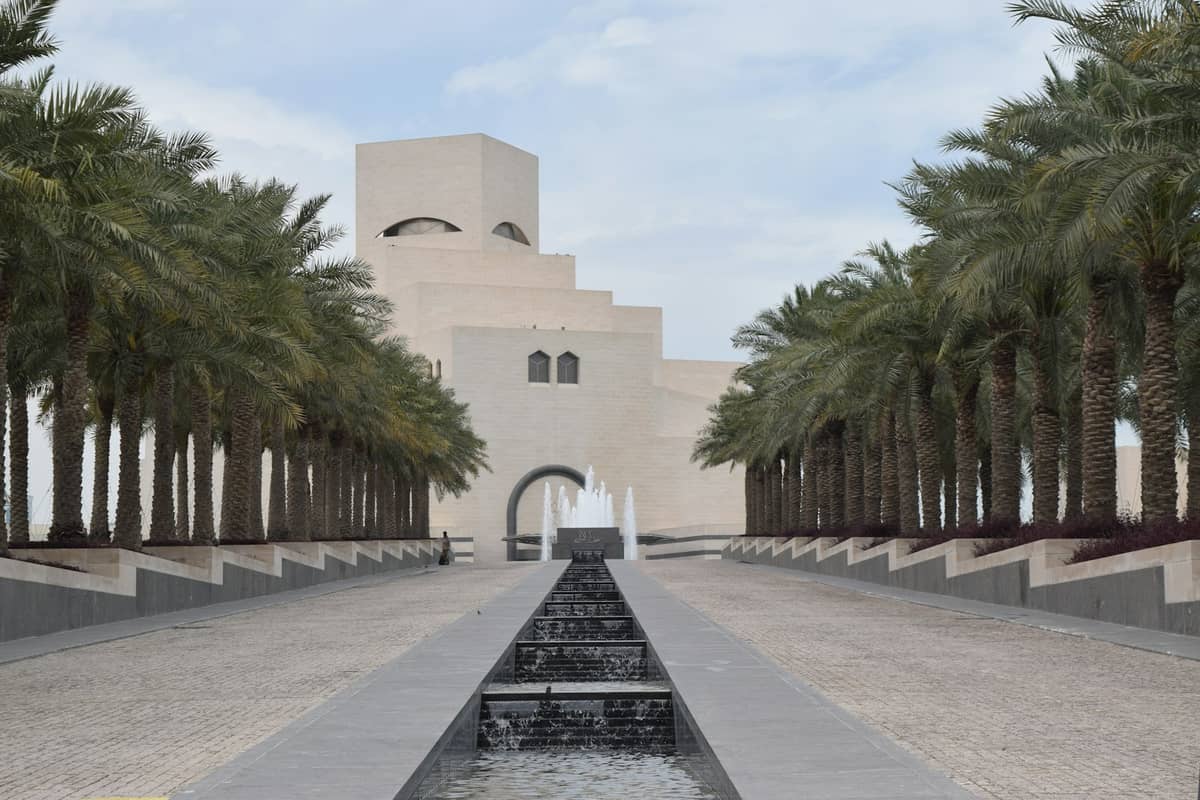 Panoramablick auf das Museum für Islamische Kunst in Doha – das Hauptgebäude, eingerahmt von Palmen und einem langen Wasserspiel, das zum Eingang führt.
