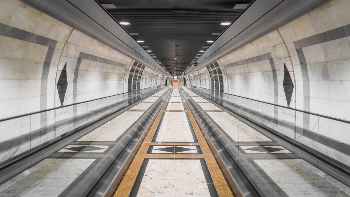 Moderner, mit Marmor verkleideter unterirdischer Metrokorridor mit Laufbändern und geometrischen Mustern, wahrscheinlich im Transportsystem von Doha.