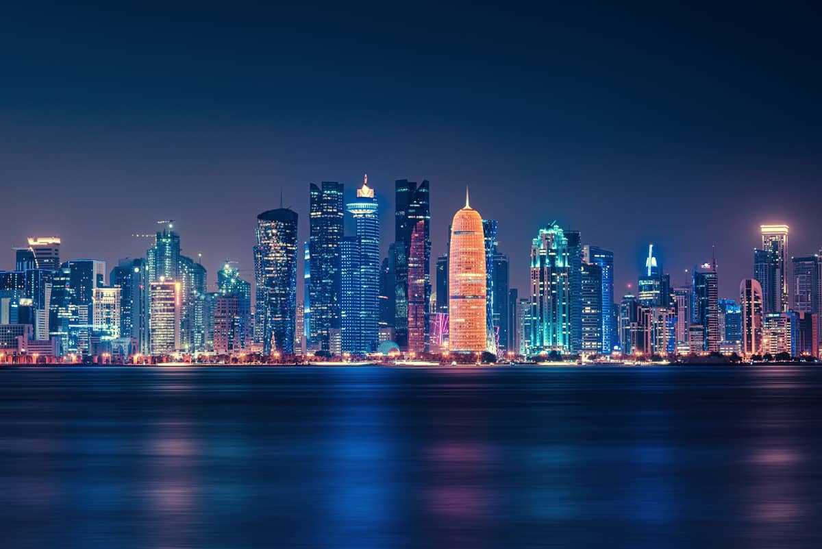 Die beleuchtete Skyline von West Bay in Doha bei Nacht, mit bunten Reflexionen auf dem Wasser der Bucht und klarem Blick auf moderne Wolkenkratzer.