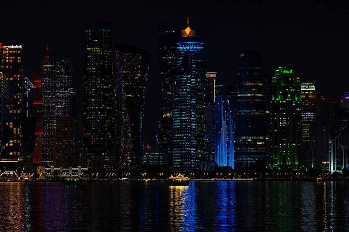 Nächtlicher Blick auf Dohas beleuchtete Skyline mit bunten Hochhäusern, die sich auf dem Wasser spiegeln.