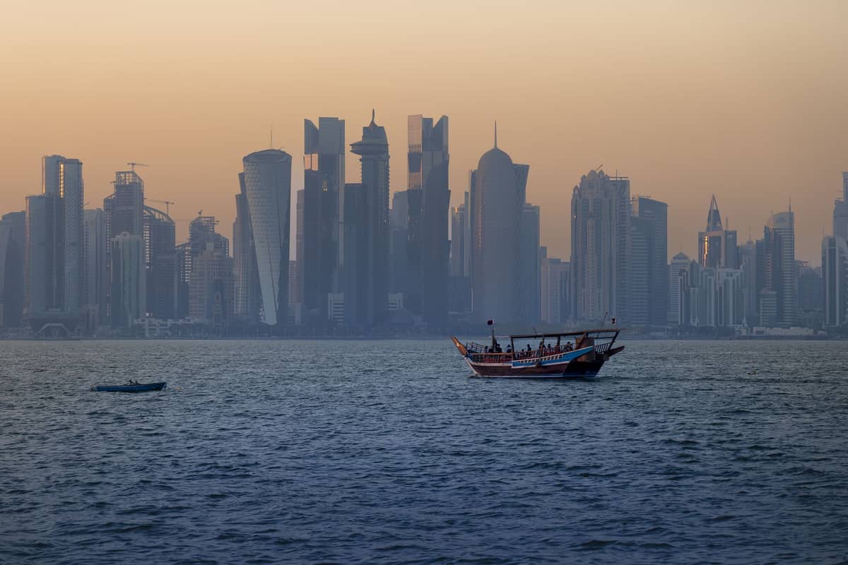 Traditionelles Dhow-Boot auf der Bucht von Doha in der Abenddämmerung mit der beleuchteten Skyline von West Bay im Hintergrund.