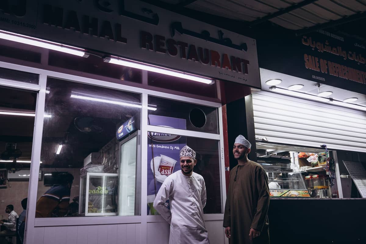 Zwei Männer stehen nachts vor einem günstigen lokalen Restaurant in einem älteren Geschäftsviertel in Doha.