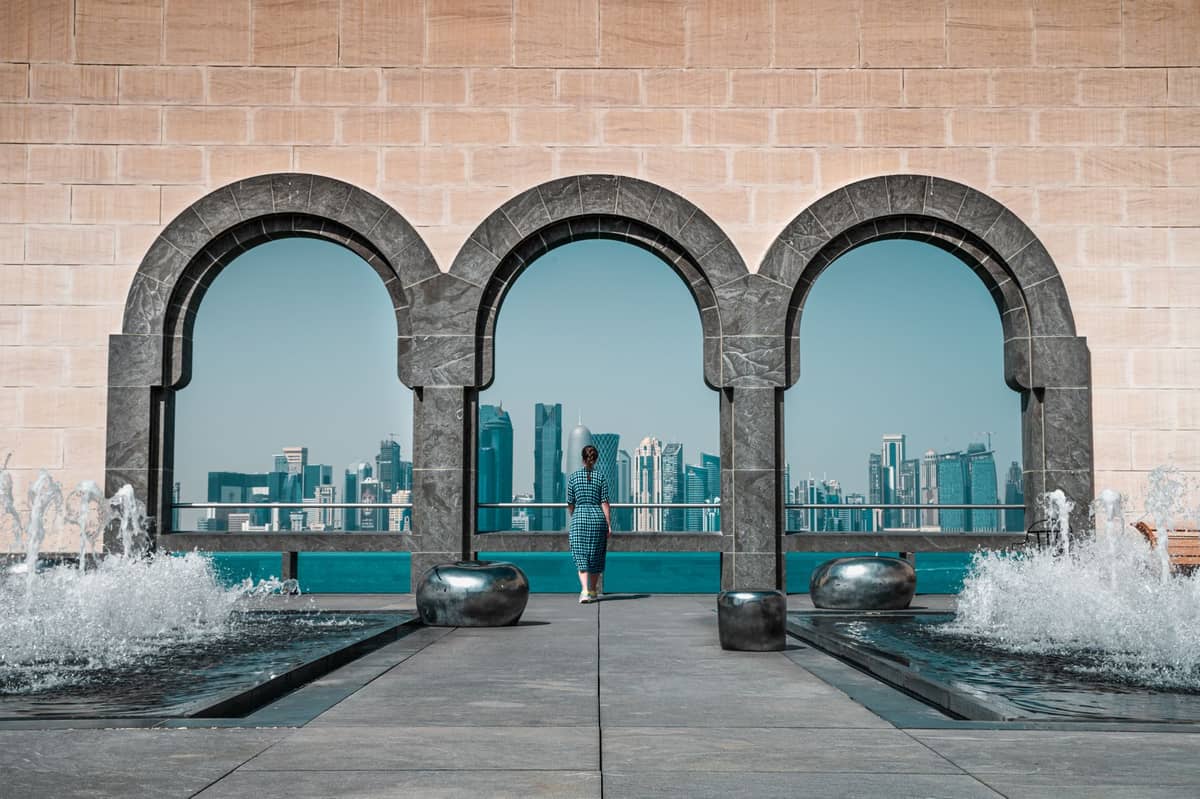 Blick auf die Skyline von Doha durch die ikonischen Bogenfenster und Springbrunnen auf der Wasserfront-Terrasse des Museums für Islamische Kunst – einer der fotogensten Orte Dohas.